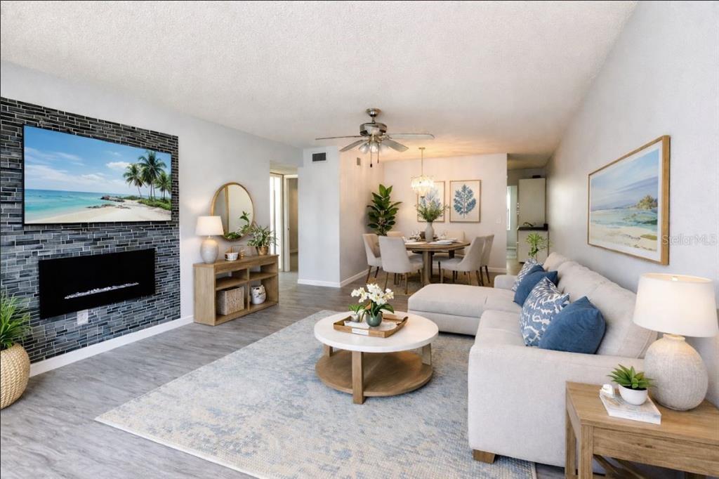 A living room with a stone fireplace, wall-mounted television, sectional sofa, and dining area — 2330 ECUADORIAN WAY UNIT 32, CLEARWATER, FL