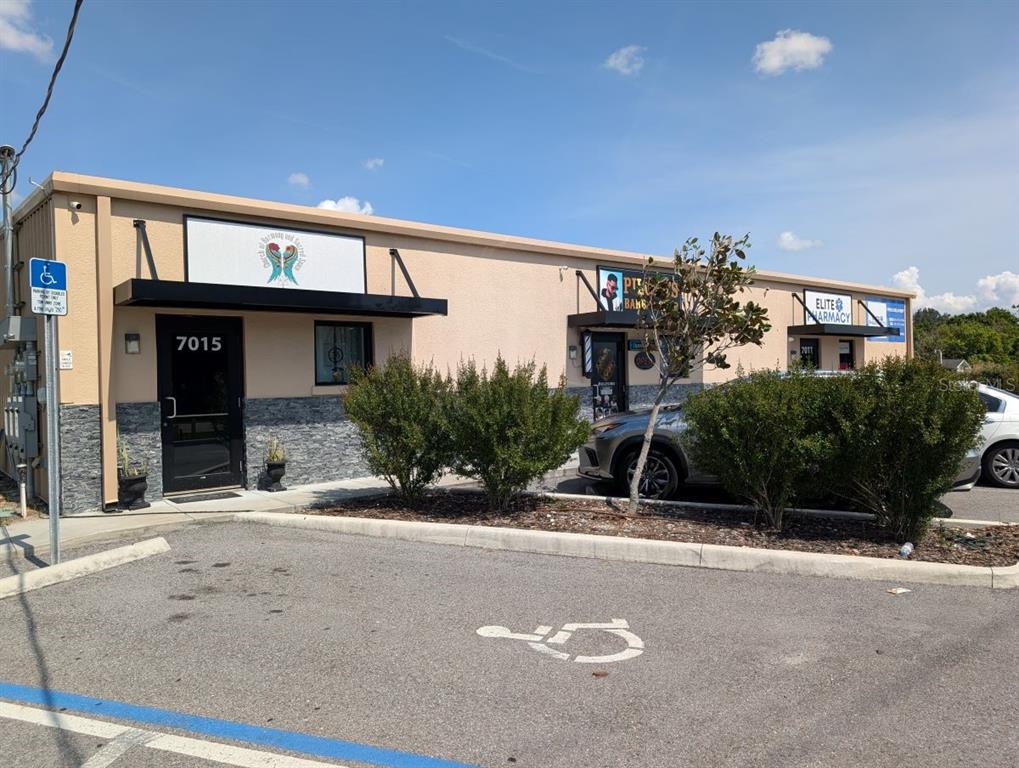 A single-story commercial building with a tan facade, stone base, and multiple storefront entrances — 7011 N MANHATTAN AVENUE, TAMPA, FL