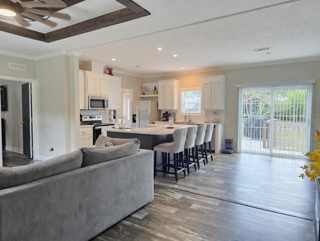 A kitchen with a central island and bar seating opens into a living room area — 10617 SKEWLEE GARDENS DRIVE, THONOTOSASSA, FL