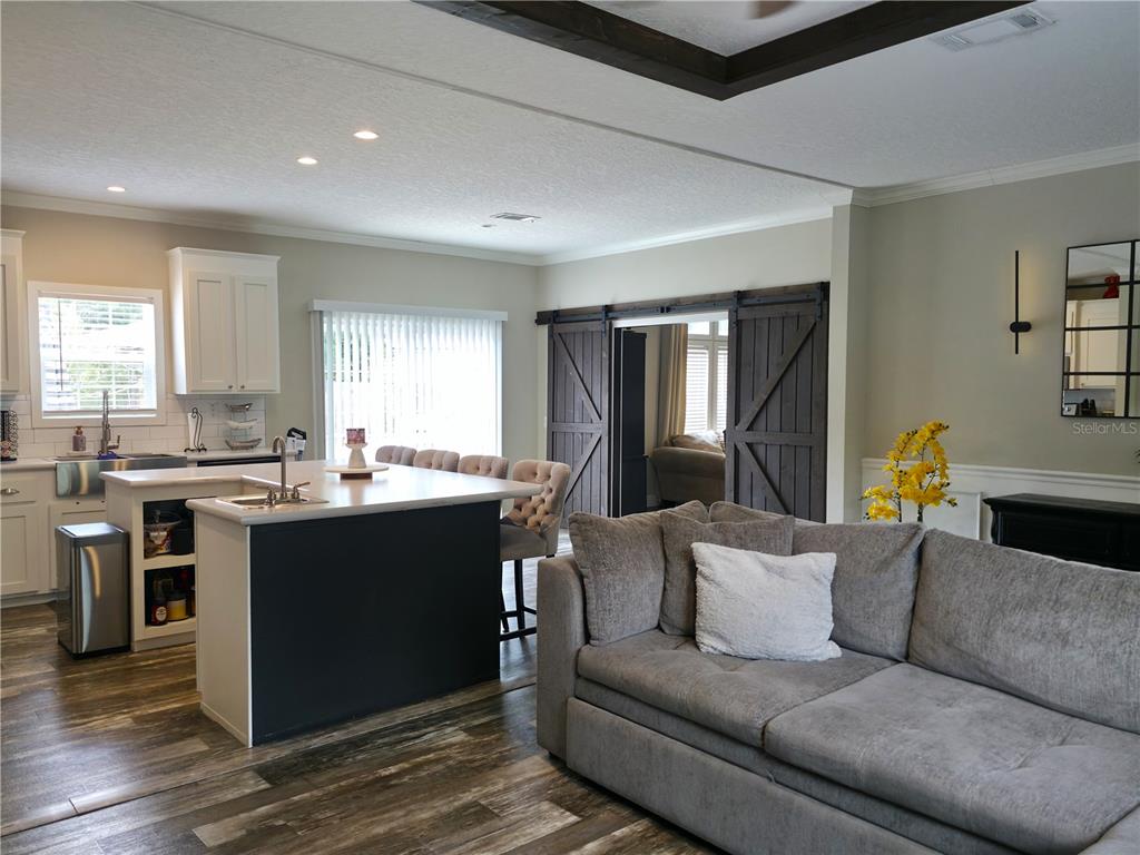 An open-concept kitchen and living area features a dark island, barn doors, and wood flooring — 10617 SKEWLEE GARDENS DRIVE, THONOTOSASSA, FL