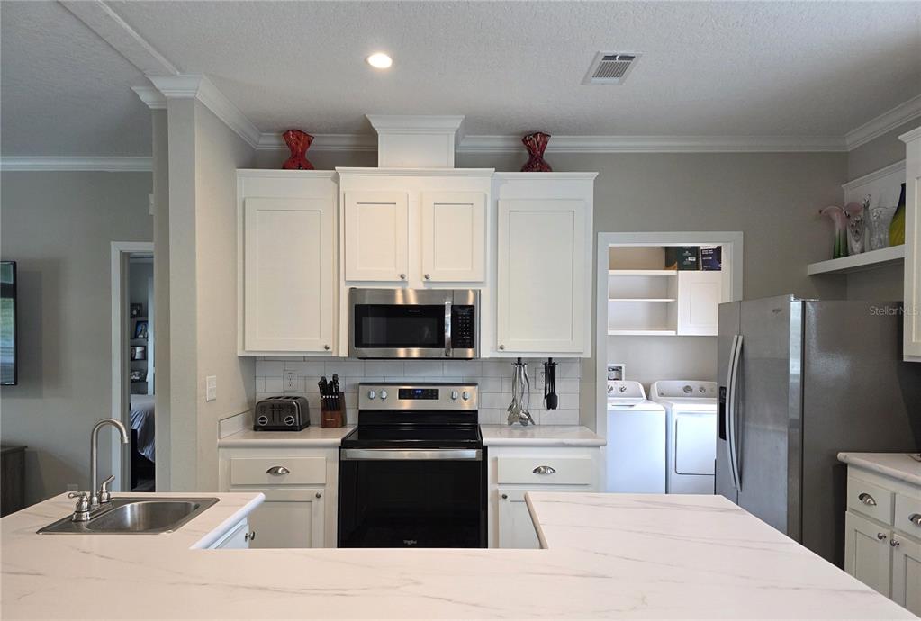 A kitchen features white cabinets, stainless steel appliances, and a white marble-patterned island countertop — 10617 SKEWLEE GARDENS DRIVE, THONOTOSASSA, FL