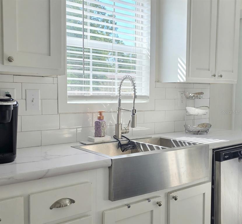 A kitchen sink area featuring a stainless steel farmhouse sink, white cabinets, and subway tile — 10617 SKEWLEE GARDENS DRIVE, THONOTOSASSA, FL