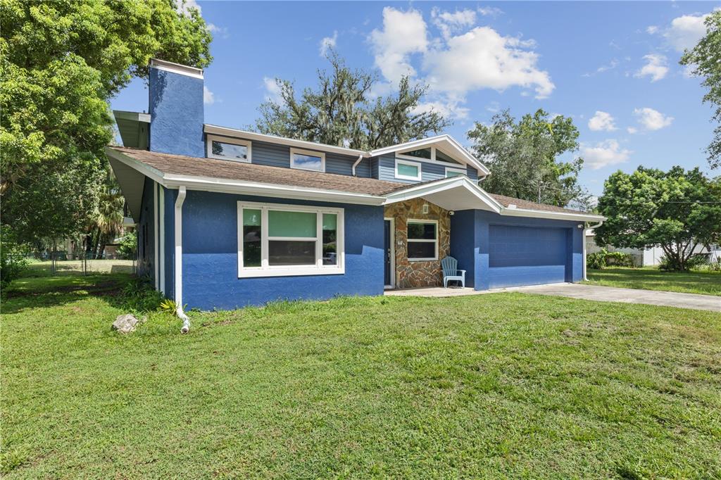 A blue two-story house with a stone entryway, a large chimney, and an attached garage — 4734 MONTEREY DRIVE, WINTER HAVEN, FL