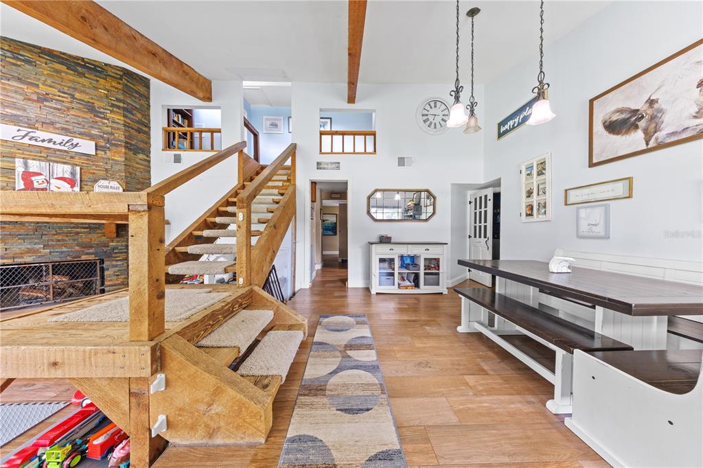A living and dining area features a stone fireplace, wooden staircase, and exposed ceiling beams — 4734 MONTEREY DRIVE, WINTER HAVEN, FL