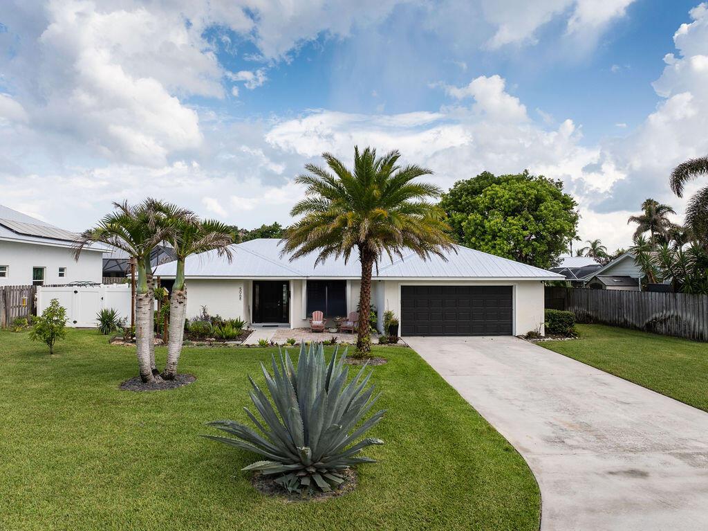 A single-story house with a white exterior, dark garage door, and palm trees in the yard — 5068 SE Major Way, Stuart FL 34997, STUART, FL