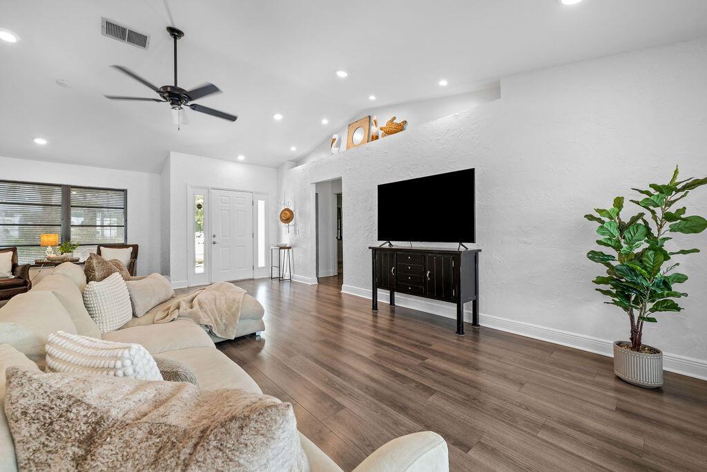 A living room features a vaulted ceiling, wood-look flooring, a sectional sofa, and a television — 5068 SE Major Way, Stuart FL 34997, STUART, FL