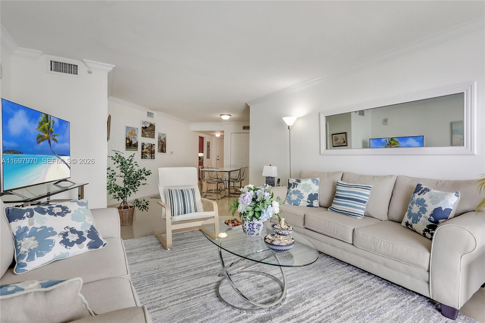 A bright living room features a beige sofa, glass coffee table, and a large wall mirror — 3000 N Ocean Dr # 10B, Riviera Beach FL 33404, RIVIERA BEACH, FL