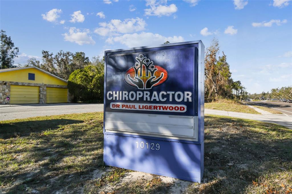 A blue freestanding sign for a chiropractor stands on a grassy lot near a building — 10129 LITTLE ROAD, NEW PORT RICHEY, FL
