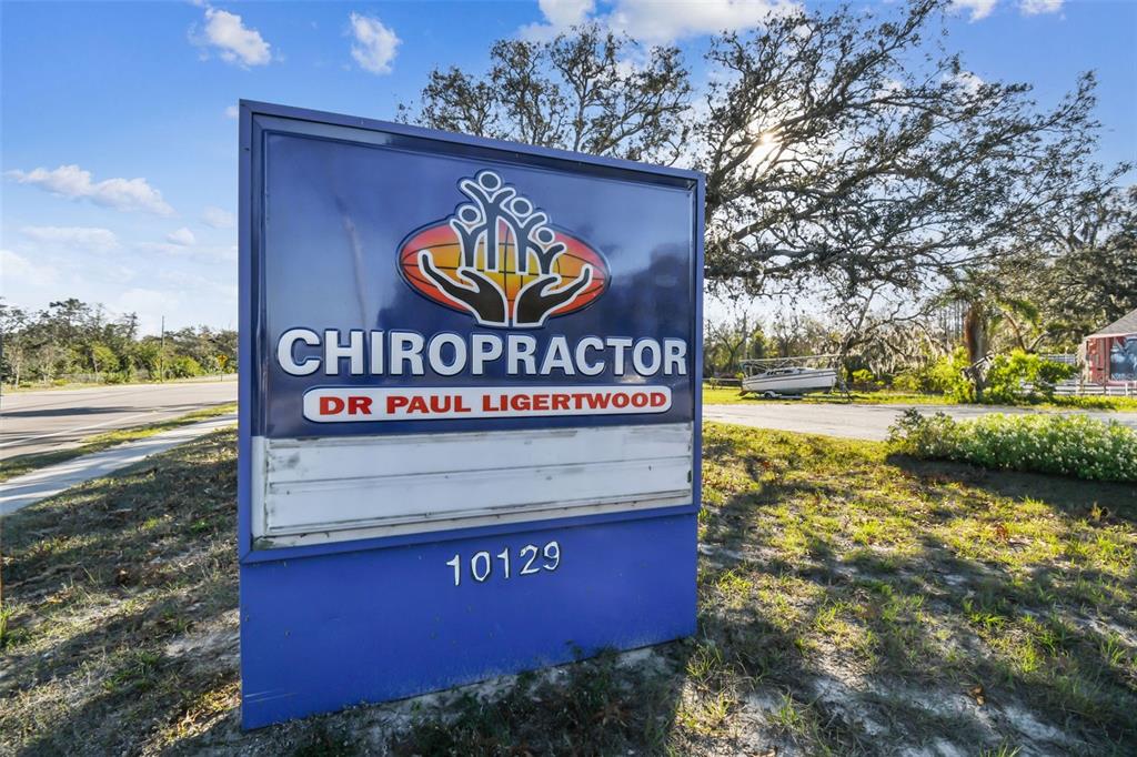 A blue sign for a chiropractor's office stands outdoors near a road and trees — 10129 LITTLE ROAD, NEW PORT RICHEY, FL
