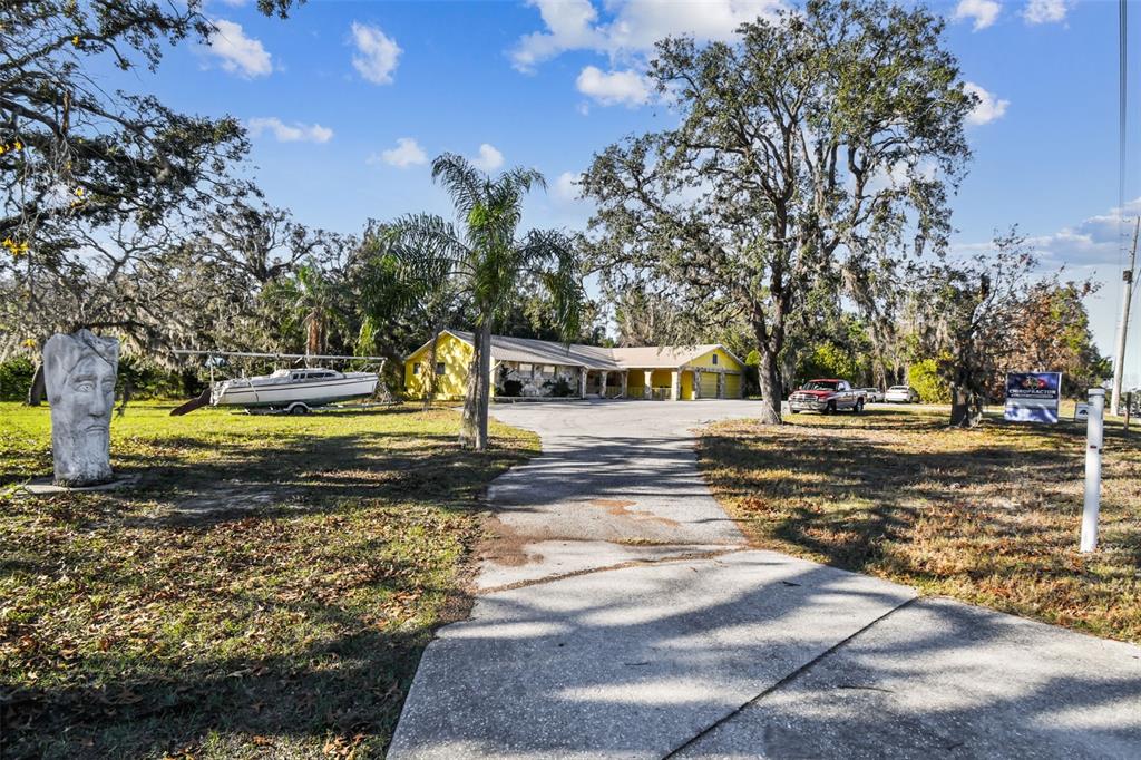 A yellow house with a long driveway, a boat on a trailer, and a stone sculpture — 10129 LITTLE ROAD, NEW PORT RICHEY, FL