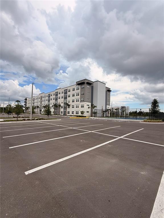 A multi-story apartment building stands behind a large, empty paved parking lot — 5579 MILLENIA PARK BOULEVARD UNIT 309, ORLANDO, FL