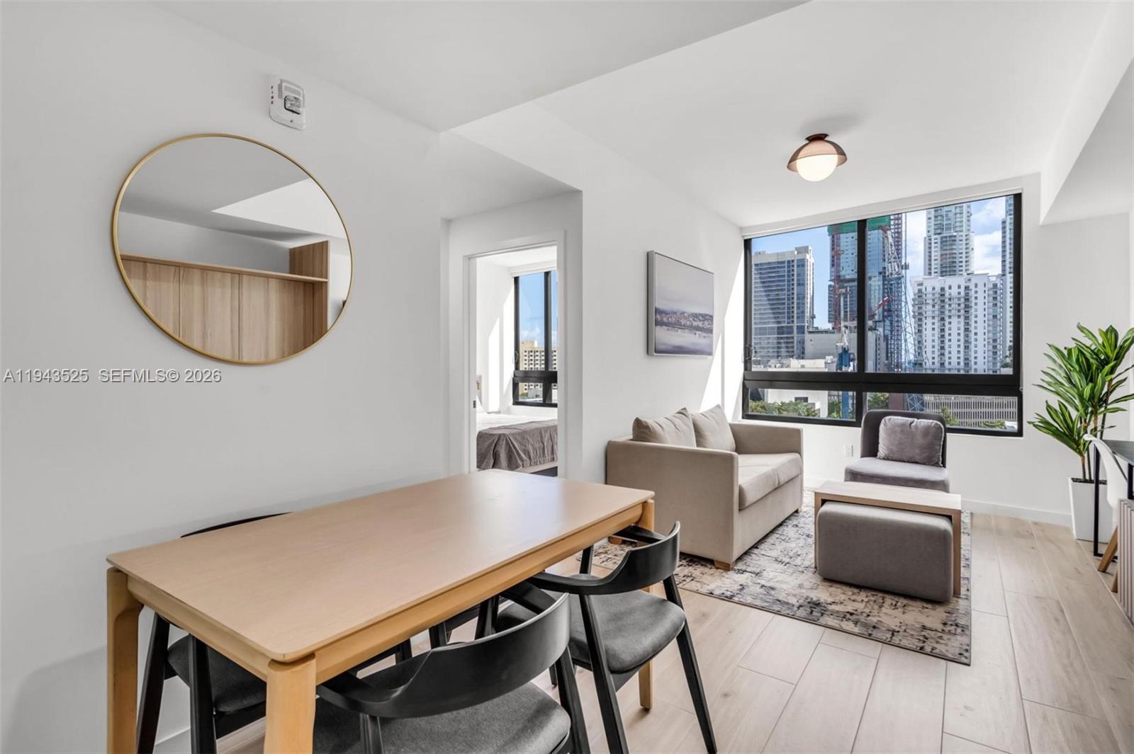 A modern living and dining area with light wood floors, neutral furniture, and city views — 225 N Miami Ave # 1005, Miami FL 33128, MIAMI, FL