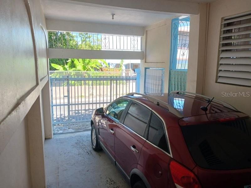 A red car is parked inside a covered carport with a metal gate — #6 CALLE 3, GUANICA, PR
