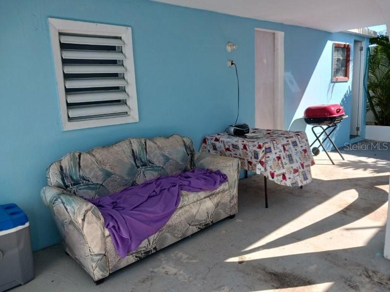 A covered outdoor patio features a patterned sofa, a table with a tablecloth, and a grill — #6 CALLE 3, GUANICA, PR