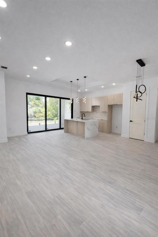 An open-concept kitchen and living area features light wood cabinetry, a marble island, and tile flooring — 1105 CORNELIUS BOULEVARD, PORT CHARLOTTE, FL