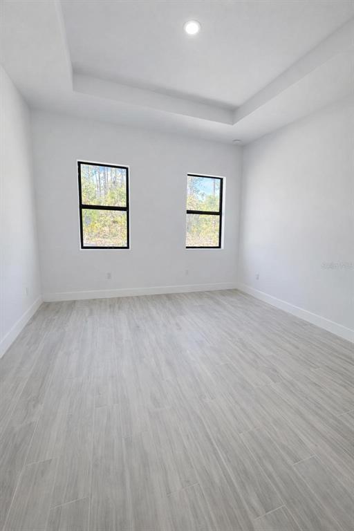 An empty room with light wood-look tile flooring, white walls, and a tray ceiling — 1105 CORNELIUS BOULEVARD, PORT CHARLOTTE, FL