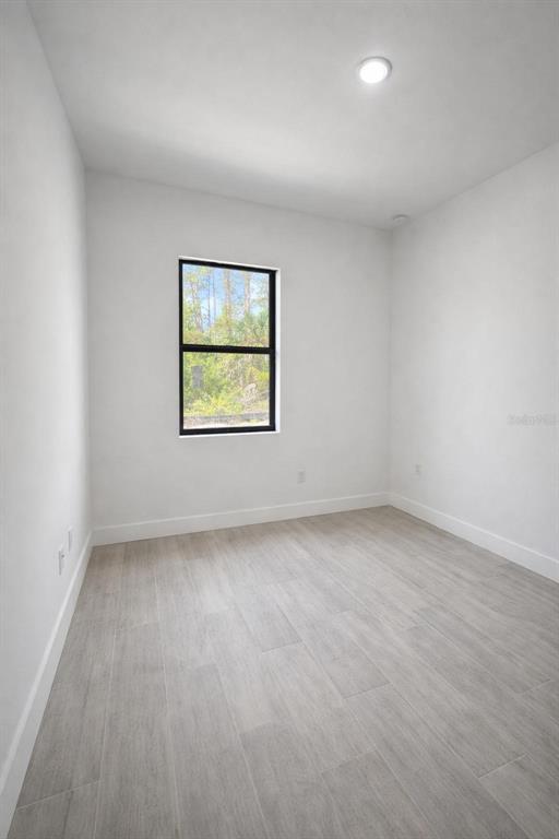 An empty room with white walls, light wood-look tile flooring, and a single window — 1105 CORNELIUS BOULEVARD, PORT CHARLOTTE, FL