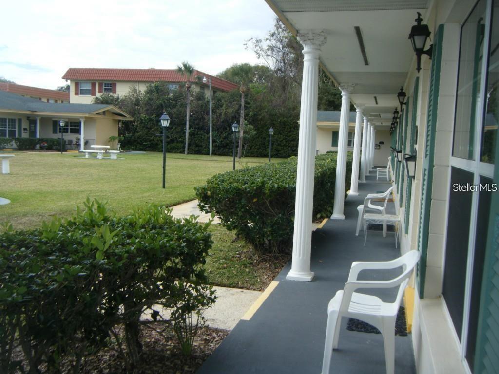 A covered outdoor walkway features white columns, plastic chairs, and a view of a lawn — 109 PERKINS STREET UNIT 9, LEESBURG, FL