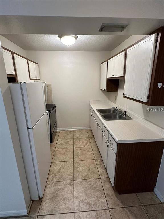 A galley kitchen features white appliances, wood-trimmed cabinets, and light-colored tile flooring — 109 PERKINS STREET UNIT 9, LEESBURG, FL
