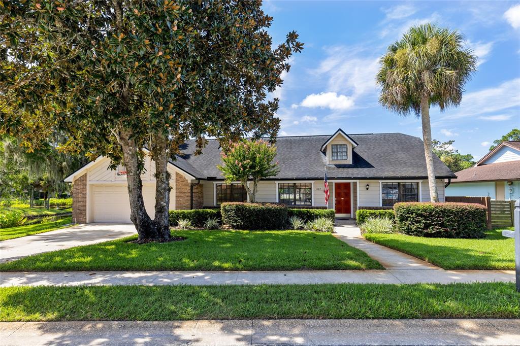 A single-story house with a dark roof, beige siding, a red front door, and large trees — 807 RIVERBEND BOULEVARD, LONGWOOD, FL