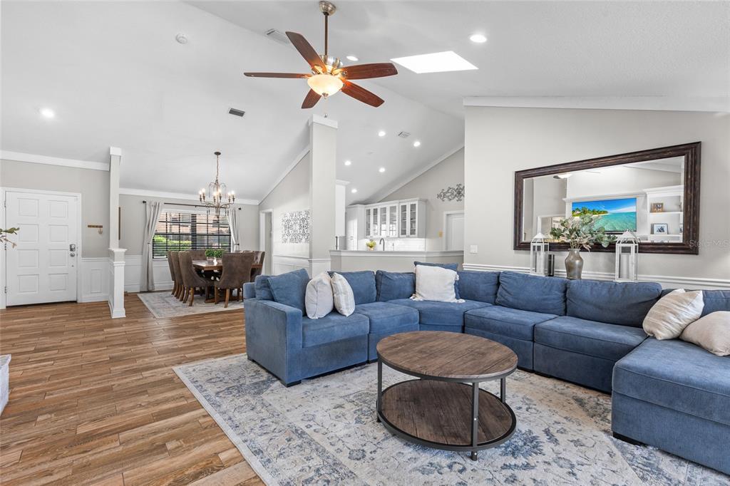 A spacious living room features a blue sectional sofa, wood flooring, and an open kitchen — 807 RIVERBEND BOULEVARD, LONGWOOD, FL