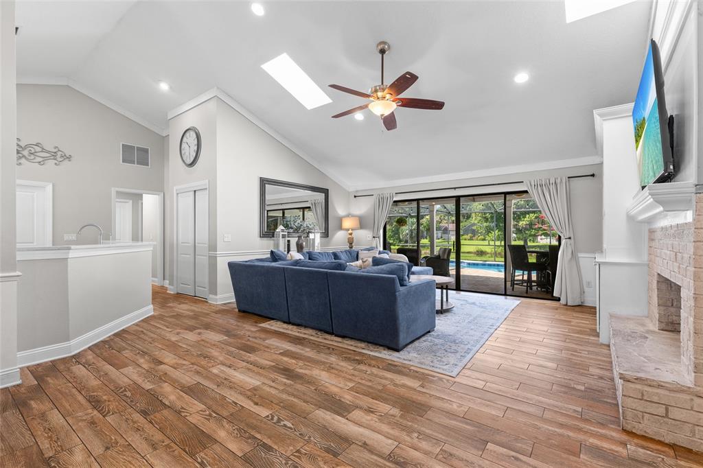 A living room with a blue sectional, vaulted ceiling, fireplace, and sliding doors to a pool — 807 RIVERBEND BOULEVARD, LONGWOOD, FL