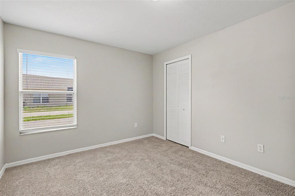 An empty bedroom with beige carpet, light gray walls, a window, and a white closet — 449 DANUBE DRIVE, KISSIMMEE, FL