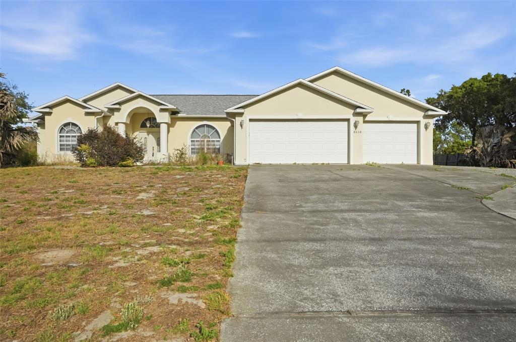 A single-story house with a beige stucco exterior, a two-car garage, and a concrete driveway — 8038 MADRID ROAD, WEEKI WACHEE, FL