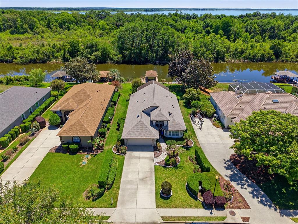 An aerial view shows three suburban houses with driveways, lawns, and docks along a canal — 6120 LANDINGS BOULEVARD, LADY LAKE, FL