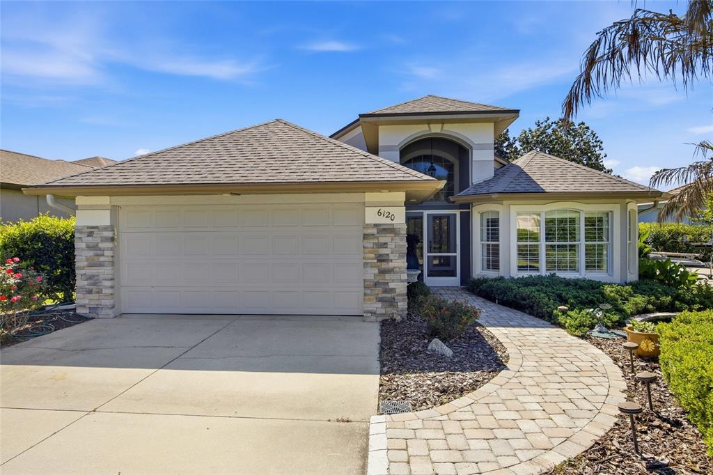 A single-story house features a two-car garage, stone accents, and a paved walkway — 6120 LANDINGS BOULEVARD, LADY LAKE, FL