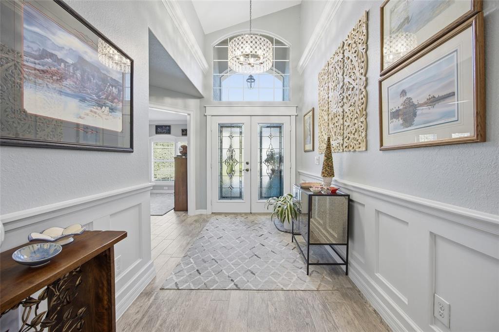 A bright entryway features a double front door, a crystal chandelier, and white wainscoting — 6120 LANDINGS BOULEVARD, LADY LAKE, FL