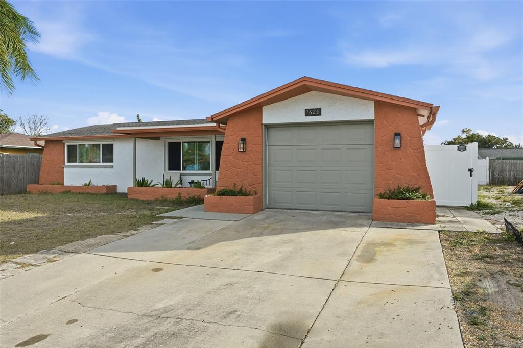 A single-story house features a white stucco facade, orange stone accents, and a concrete driveway — 7628 DALE DRIVE, PORT RICHEY, FL