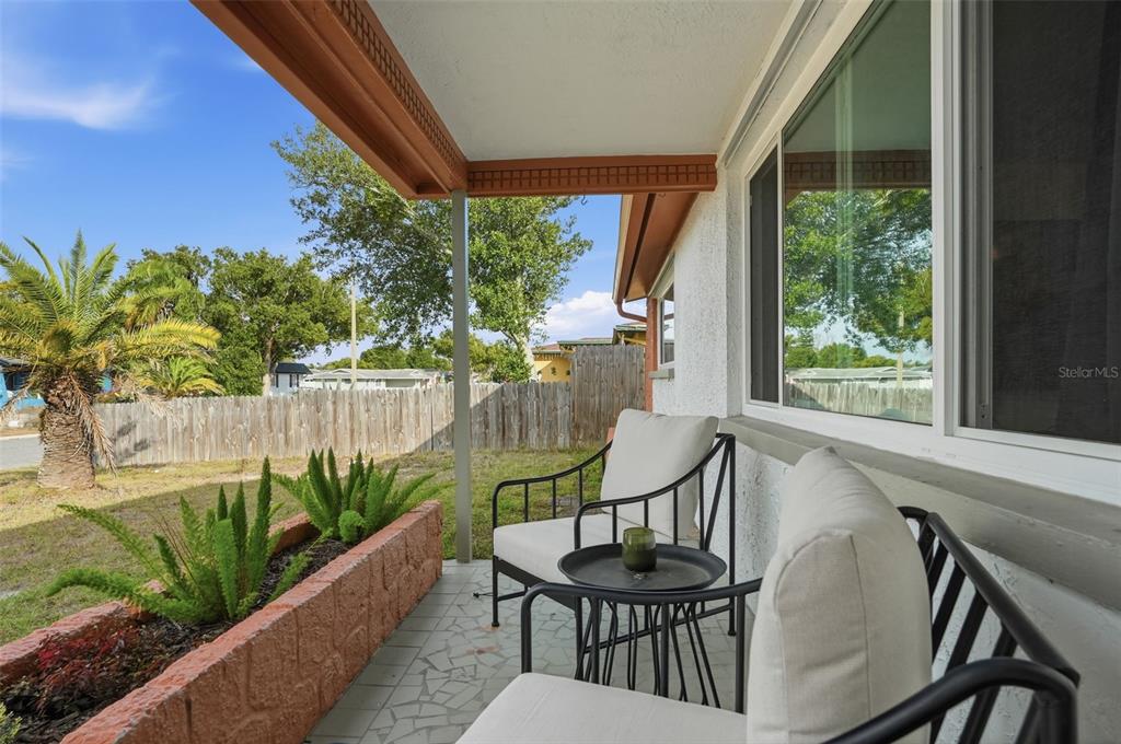 A covered patio features a stone planter, two chairs, and a small table — 7628 DALE DRIVE, PORT RICHEY, FL