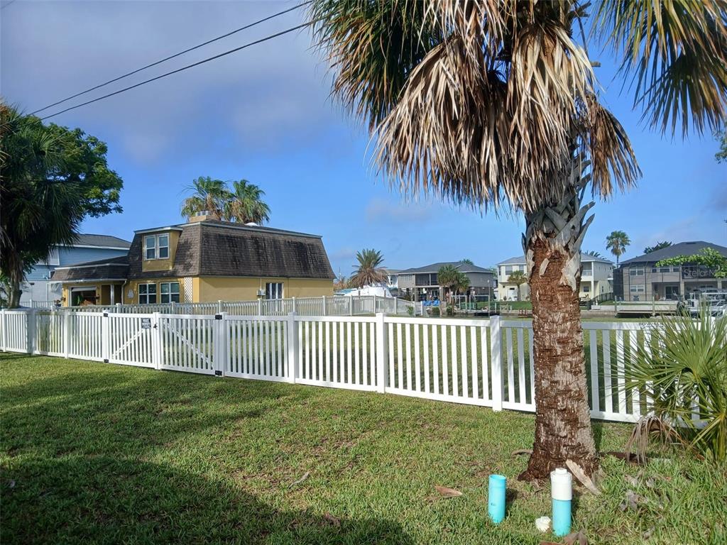 A white vinyl fence encloses a grassy yard in front of a yellow waterfront house — 4489 BURMUDA DRIVE, HERNANDO BEACH, FL