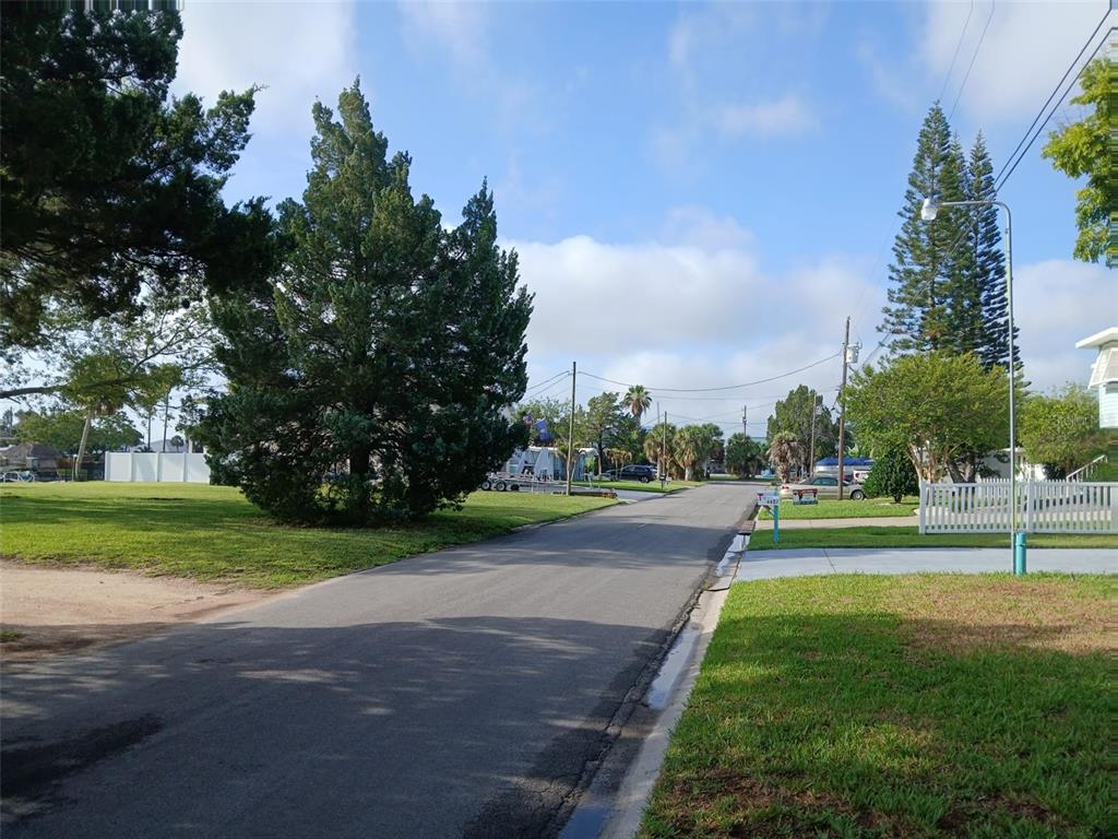 A paved residential street is lined with green lawns, mature trees, and a white fence — 4489 BURMUDA DRIVE, HERNANDO BEACH, FL