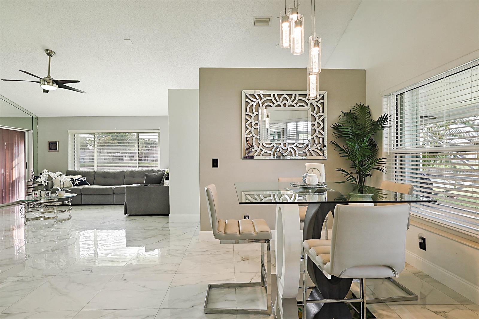 A dining area with a glass table and chairs sits beside a living room — 7852 Lake Champlain Court, Delray Beach FL 33446, DELRAY BEACH, FL