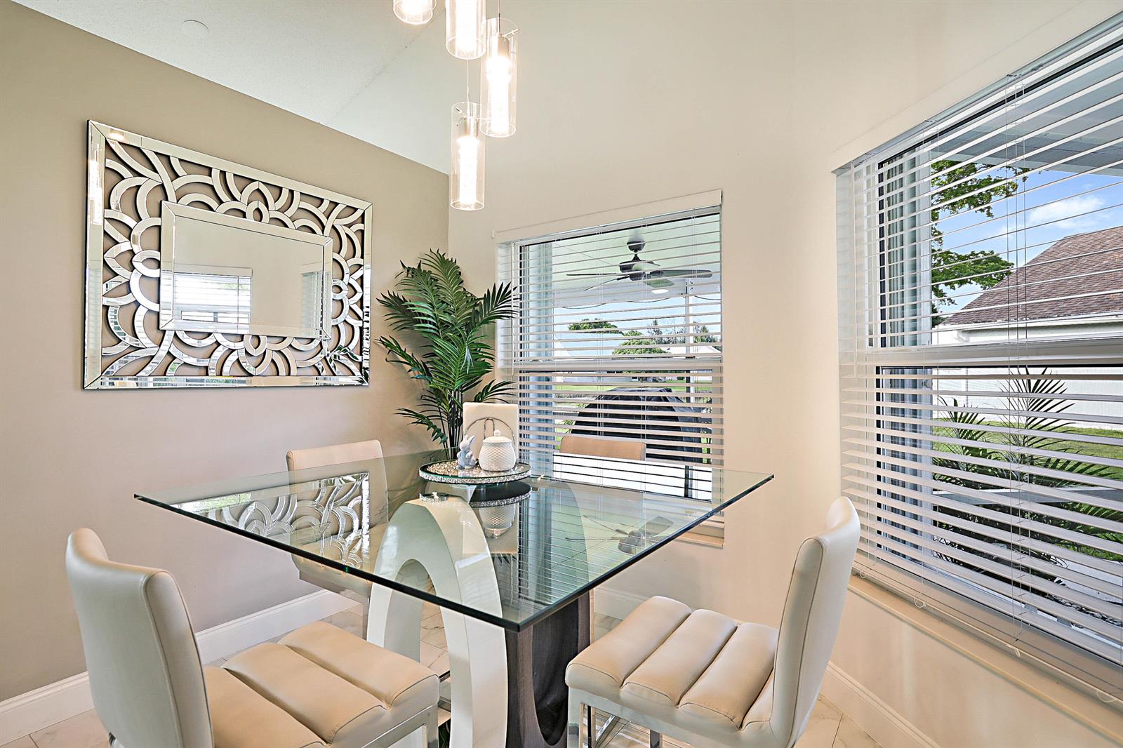A dining area features a glass-top table, four cream chairs, a decorative mirror, and windows — 7852 Lake Champlain Court, Delray Beach FL 33446, DELRAY BEACH, FL