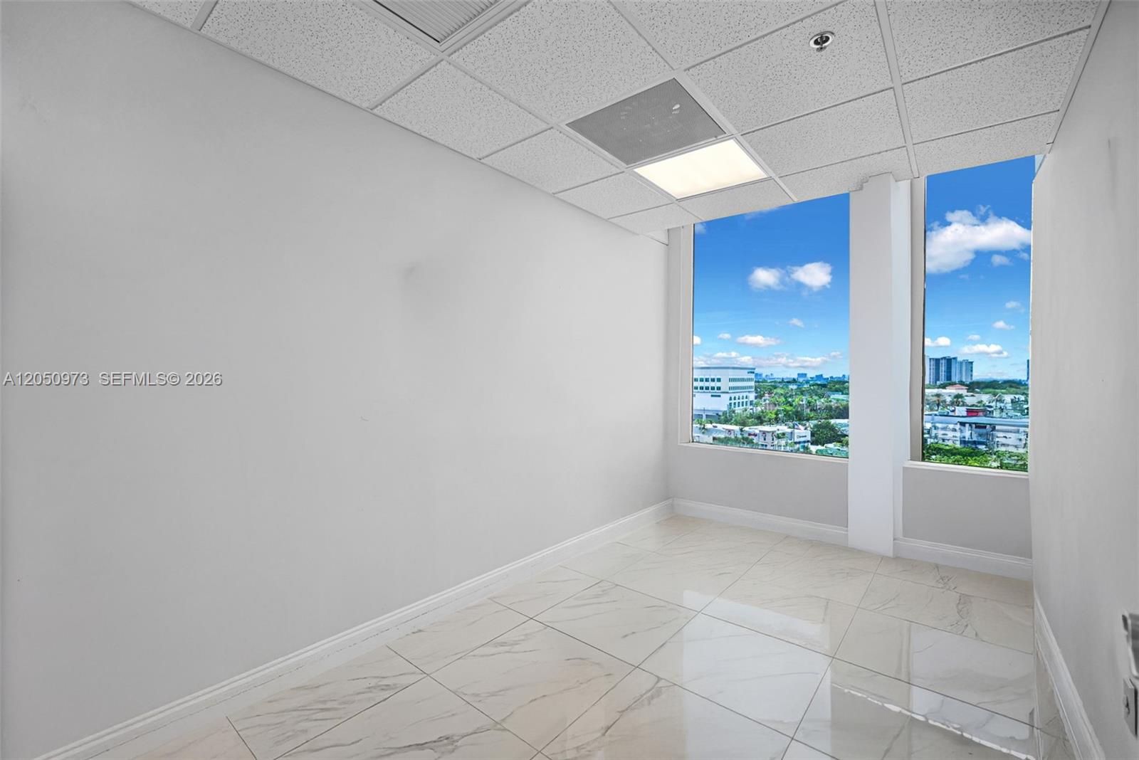 An empty office space features white walls, marble-patterned tile floors, and large windows with views — 12550 Biscayne Blvd # 702, North Miami FL 33181, NORTH MIAMI, FL