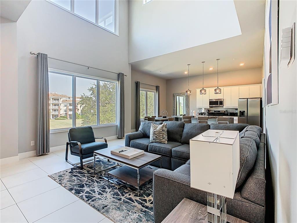 A living room with high ceilings, a grey sectional sofa, and an open-concept kitchen — 7740 SANDY RIDGE DRIVE UNIT 245, REUNION, FL