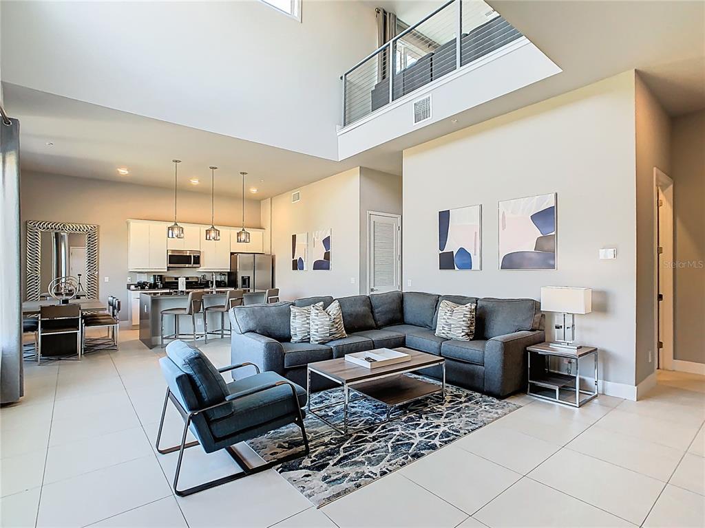 A modern open-concept living room and kitchen feature high ceilings, tile floors, and gray furniture — 7740 SANDY RIDGE DRIVE UNIT 245, REUNION, FL