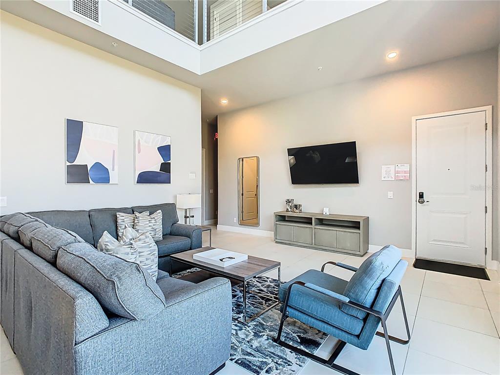 A living room features a grey sectional sofa, blue armchair, television, and high ceilings — 7740 SANDY RIDGE DRIVE UNIT 245, REUNION, FL