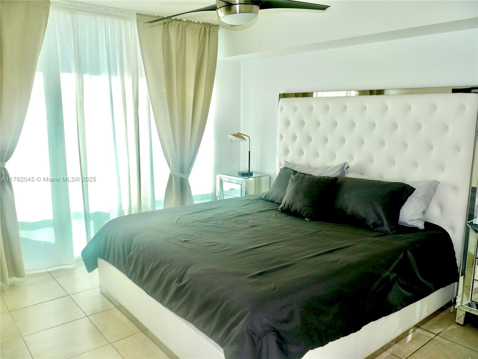 A bedroom features a tufted white headboard, black bedding, and floor-to-ceiling curtains — 31 SE 5th St # 2611, Miami FL 33131, MIAMI, FL