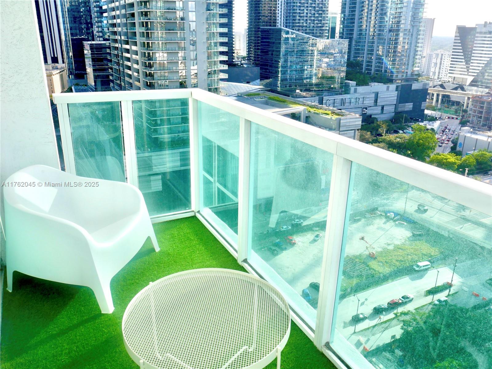 A high-rise balcony features artificial turf, a white chair, a round table, and glass railings — 31 SE 5th St # 2611, Miami FL 33131, MIAMI, FL
