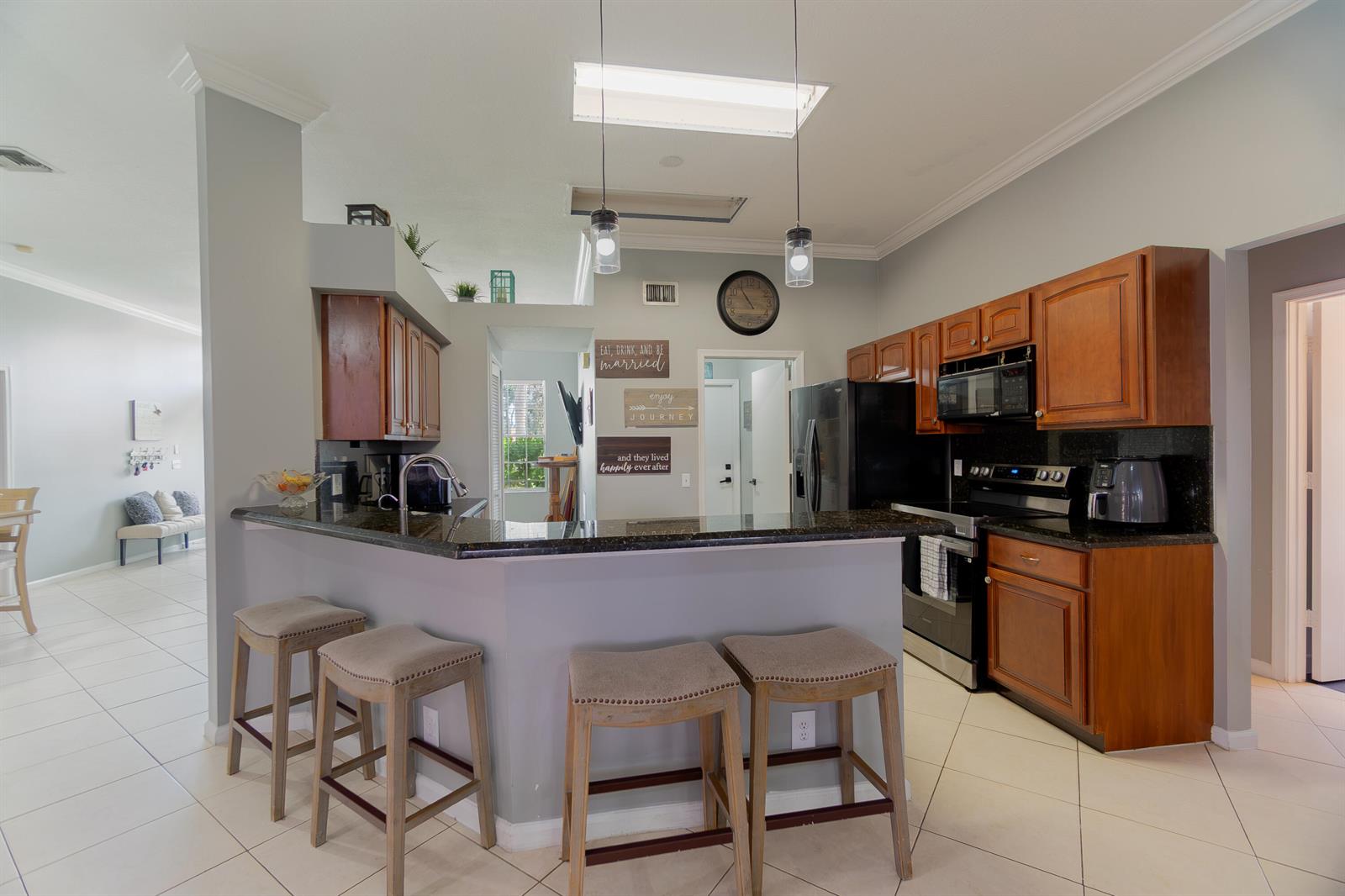 A kitchen features wood cabinets, a dark granite breakfast bar with four stools, and tile flooring — 149 Cove Road, FL 33413, FL