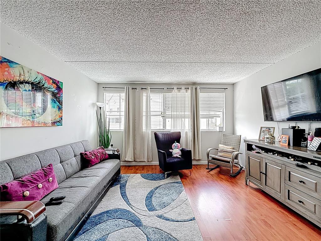 A living room features a gray sofa, a dark armchair, a rocking chair, and wood flooring — 6065 NW 186TH STREET UNIT 312, HIALEAH, FL