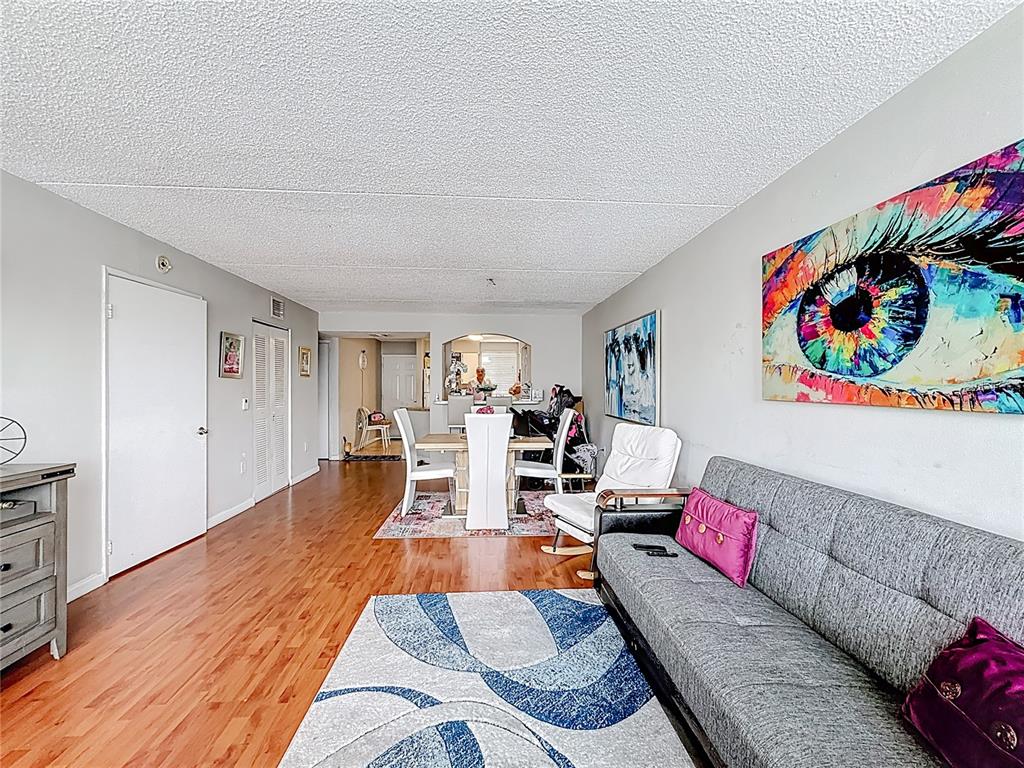 A living and dining area features hardwood floors, a gray sofa, and colorful wall art — 6065 NW 186TH STREET UNIT 312, HIALEAH, FL