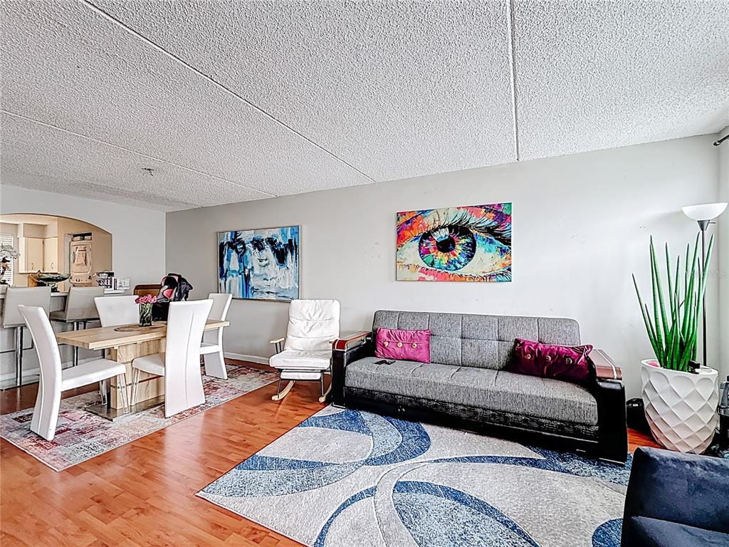 A living and dining area features wood flooring, a grey sofa, and colorful wall art — 6065 NW 186TH STREET UNIT 312, HIALEAH, FL