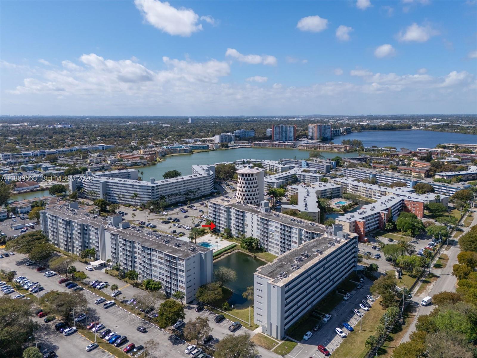 An aerial view shows multiple apartment buildings surrounding a small pond and swimming pool — 1770 NE 191st St # 1, Miami FL 33179, MIAMI, FL