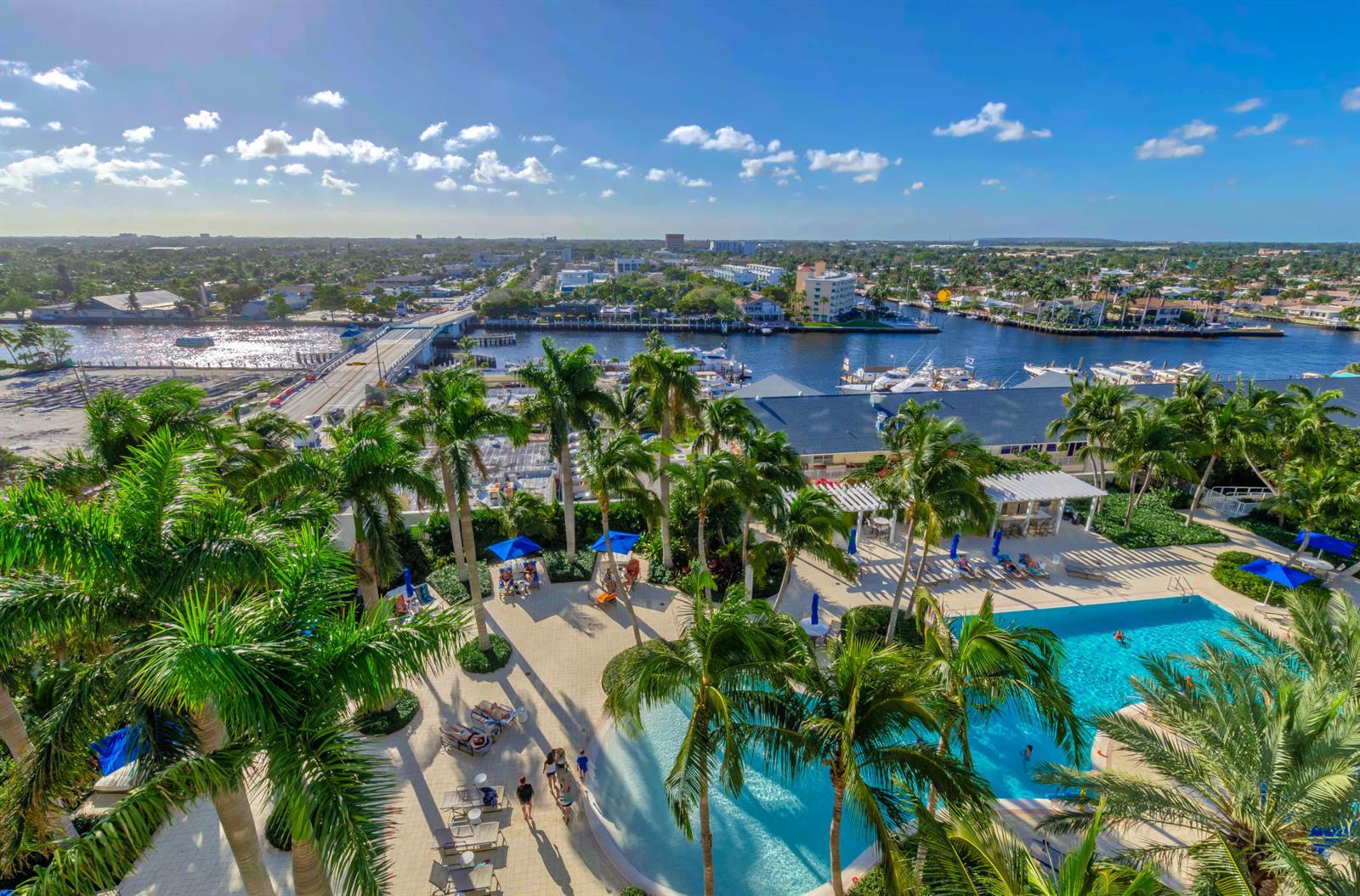 An aerial view of a resort pool deck with palm trees overlooking a waterway and bridge — 1 N Ocean Boulevard # 913, Pompano Beach FL 33062, POMPANO BEACH, FL