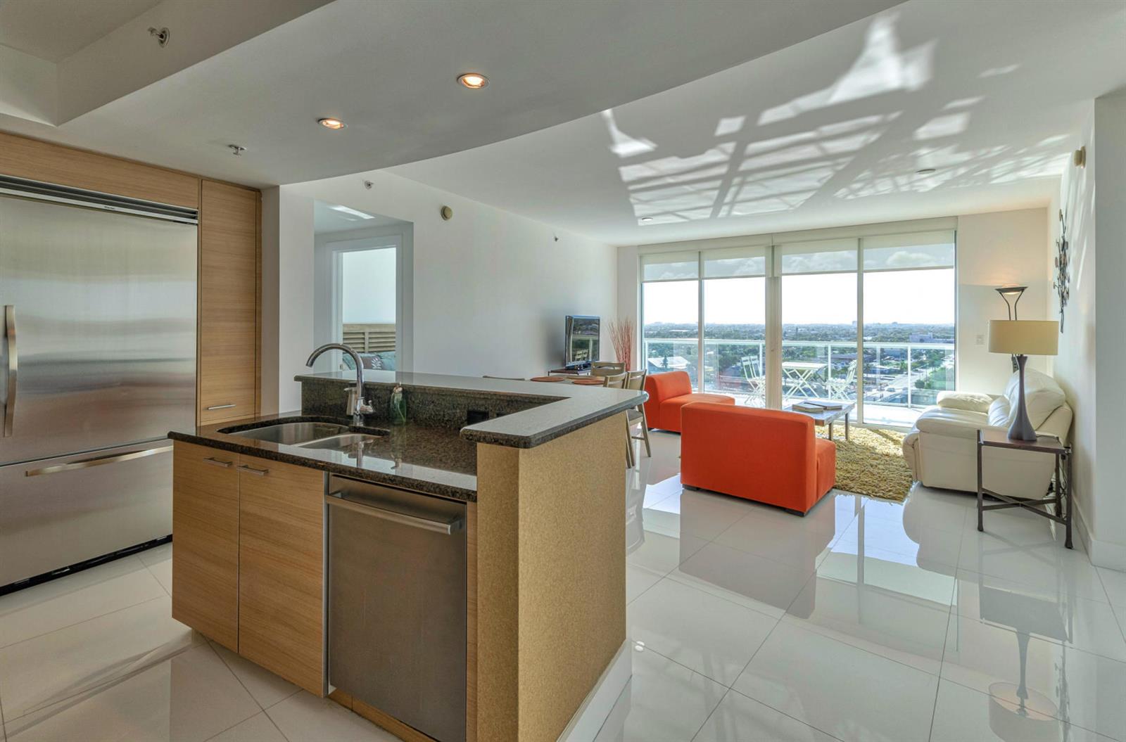 A modern kitchen with stainless steel appliances overlooks a living area with orange chairs and balcony — 1 N Ocean Boulevard # 913, Pompano Beach FL 33062, POMPANO BEACH, FL